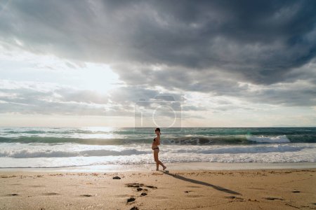 Téléchargez les photos : Femme enceinte en contemplation près du rivage, se prélassant dans la lumière de l'heure dorée - en image libre de droit