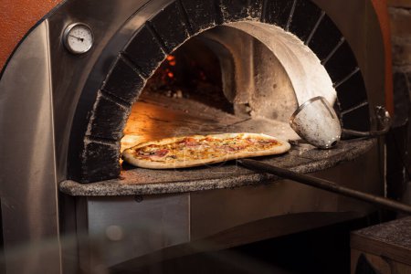 Téléchargez les photos : Un four en pierre rayonne de chaleur tandis qu'un chef récupère une pizza parée de fromage fondu et de garnitures riches, prête à servir - en image libre de droit