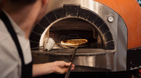 Photo for A chef skillfully slides a pizza into a wood-fired oven, showcasing the blend of tradition and modern culinary techniques - Royalty Free Image