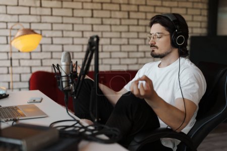 Photo for A podcaster sits contemplatively in his studio, headphones on, preparing mentally before beginning a recording session - Royalty Free Image