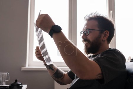 Photo for A photographer holds up film negatives to the light, observing the illuminated memories captured within each frame in his studio - Royalty Free Image