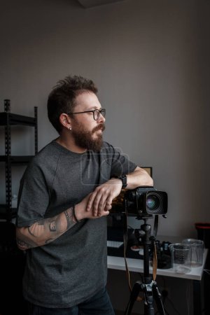 A contemplative photographer leans on his tripod-mounted camera, poised and ready for the decisive moment in his studio