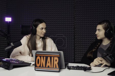 Deux femmes dans un échange ciblé lors d'un podcast en direct, avec un panneau On Air illuminant leur interaction professionnelle et dynamique dans un environnement studio