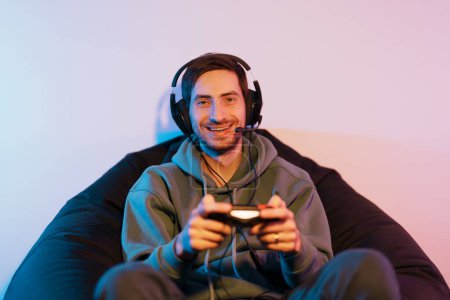 Photo for A cheerful man enjoys his gaming session, comfortably lounging in a beanbag with a controller in hand - Royalty Free Image