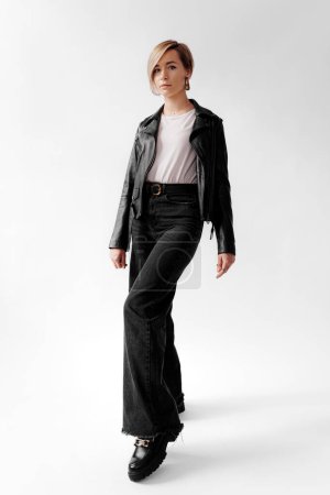 A poised young woman stands confidently in a leather jacket and flared jeans, embodying urban chic