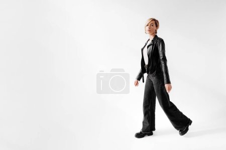 A young woman strides forward in a timeless black leather jacket and flared jeans, exuding a cool confidence