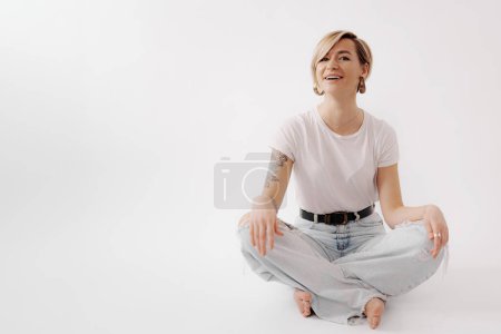 Beaming with joy, a young woman sits cross-legged in light denim, embodying casual elegance and lively spirit
