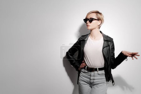 Confident young woman in a leather jacket and stylish sunglasses strikes a pose with a dramatic shadow play