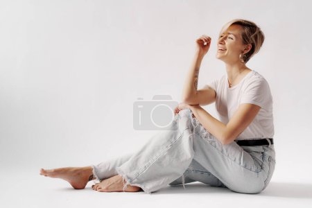 Capturing a moment of laughter, a young woman in light denim jeans and a white t-shirt enjoys a relaxed sitting pose