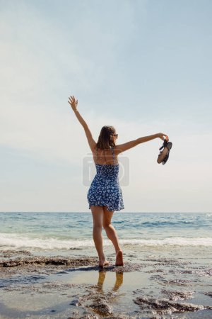 A woman dances freely on the beach, her dress and hair swept up in the invigorating sea breeze