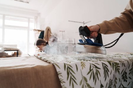 Eine Frau benutzt in ihrem sonnenbeschienenen Nähstudio ein Dampfbügeleisen auf Stoff.