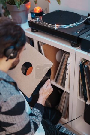 Audiophile with headphones selects a vinyl record from a shelf to play on a turntable.