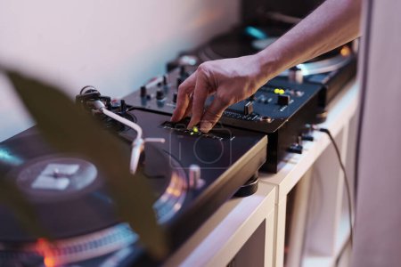 Nahaufnahme einer Hand eines DJs beim Einstellen von Einstellungen auf einem Plattenspieler während eines Live-Musik-Sets.