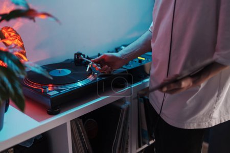 Primer plano de un DJs manos mezclando pistas en un tocadiscos de vinilo con luces led.