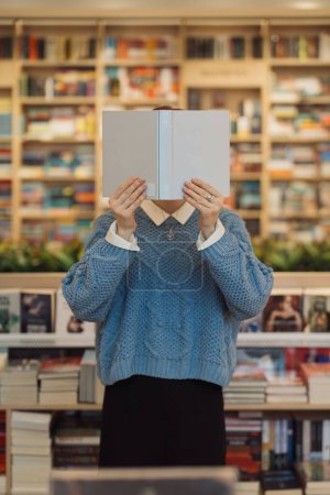 Eine nicht identifizierbare Person mit einem Buch vor dem Gesicht in einer Bibliothek.