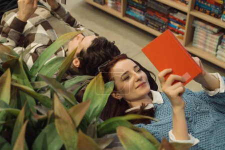 Young couple relaxing among plants in a bookstore browsing books together.