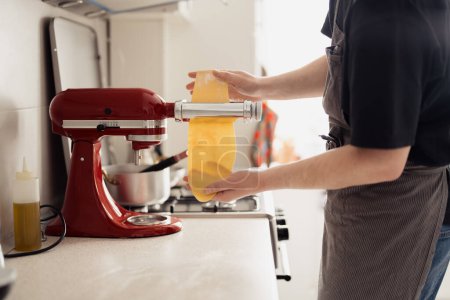 Close-up of hands using a stand mixer to prepare fresh pasta dough in a home kitchen.