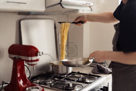 Person cooking spaghetti in a stainless steel pan on a gas stove in a tidy kitchen.