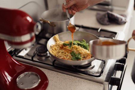 Pouring sauce over pasta in a pan, home cooking concept, kitchen setting