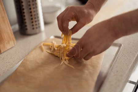 Photo for Close-up of hands places the pasta on a baking sheet in a kitchen, cooking prep concept - Royalty Free Image