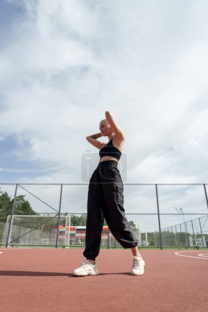 Young female athlete standing on a basketball court, resting after a workout on a sunny day, exuding confidence and strength.