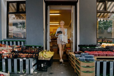 Una pequeña tienda de comestibles local ofrece una selección de productos frescos que incluyen frutas, verduras y bayas en un pintoresco entorno de barrio.