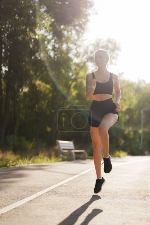 Una corredora en forma disfrutando de una caminata matutina en un parque sereno, rodeado de exuberante vegetación y suave luz matutina.