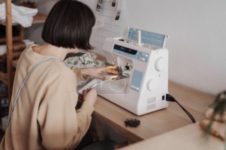 Una mujer enfocada de 35 años se está adaptando con una máquina de coser en un taller bien organizado.