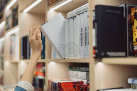 En una biblioteca moderna bien iluminada, un adulto joven es capturado eligiendo un libro de.