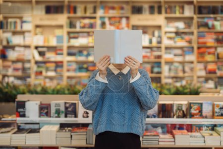 A young woman holds a book in front of her face cover, standing amidst a vibrant and varied bookstore. Shelves of books create a cozy, intellectual backdrop.
