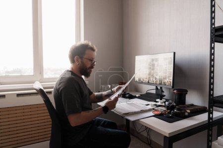 Ein fokussierter Fotograf analysiert Filmnegative in einem gut beleuchteten, modernen Home Office, umgeben von Fotoausrüstung.