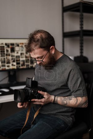 Un photographe masculin en tenue décontractée examine un appareil photo vintage à l'intérieur, mettant en valeur sa passion pour la photographie et son expertise.
