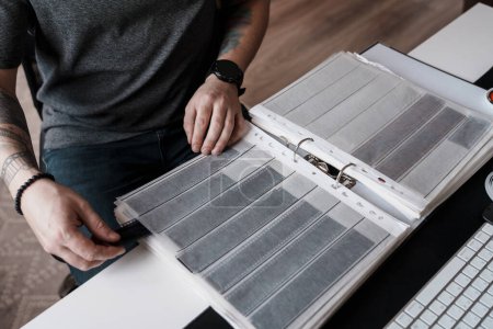 A person carefully examines film strips laid out in a binder on a office desk, epitomizing the meticulous nature of film photography.