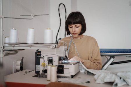 A 35-year-old woman attentively sews clothing in her cozy workshop.