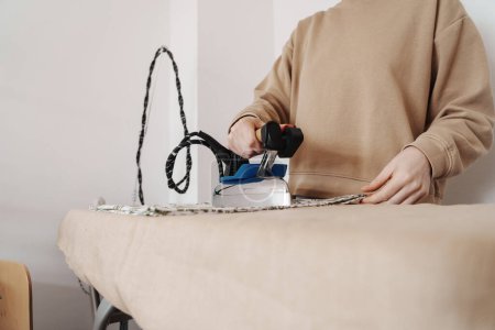 Eine Frau bügelt in ihrer Nähwerkstatt vorsichtig Stoff auf einem Bügelbrett.