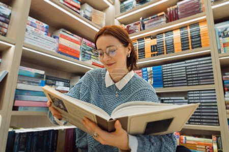 A young woman with glasses reads an interesting classic novel in a well-stocked cozy bookstore, surrounded by diverse literature genres.