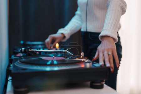 Primer plano de una hembra DJs manos ajuste de vinilo en el tocadiscos, estableciendo el ambiente de la fiesta.