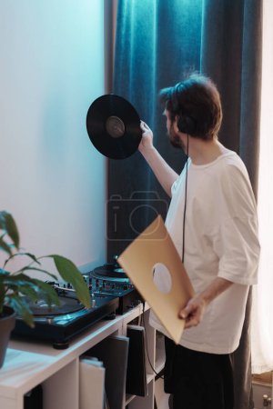 Audiophile with headphones examining a vinyl record indoors. Home entertainment concept.