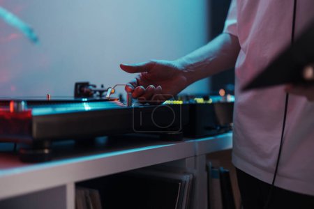 Primer plano de una mano de DJs en un tocadiscos, tocando música en una fiesta vibrante.