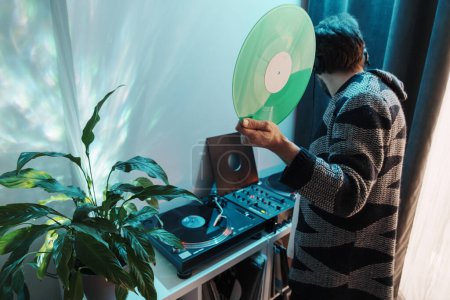 A cozy indoor scene with someone handling a vinyl record by a turntable and houseplant.