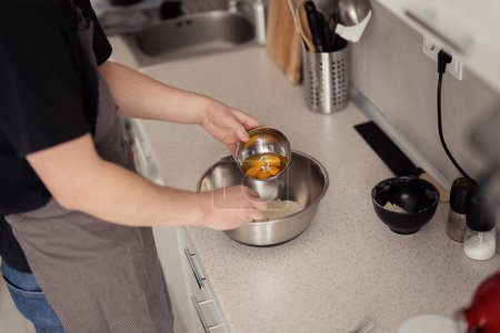 Téléchargez les photos : Gros plan des mains craquant des œufs dans un bol en acier inoxydable dans une cuisine maison. - en image libre de droit