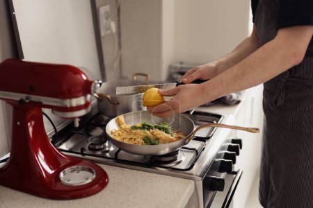 Großaufnahme der Hände, die in der heimischen Küche Zitrone auf Pasta schwenken.