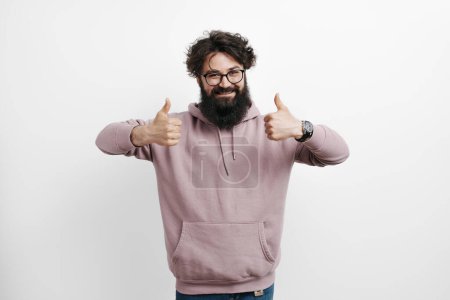 Positive young male in a stylish pink hoodie showing approval with both thumbs up. Representing concepts of satisfaction, approval, and casual fashion on a clean background.