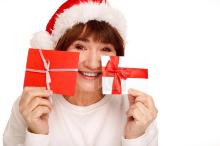 Photo for Happy middle aged mature woman in white winter clothes holds two gift vouchers isolated on white background. People holidays lifestyle concept. - Royalty Free Image