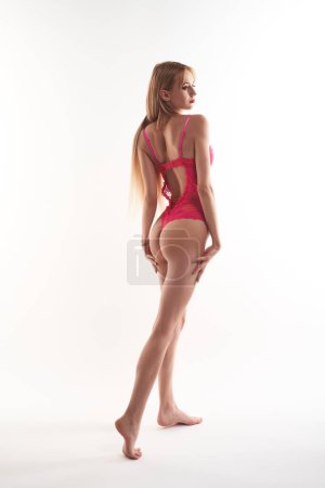 Téléchargez les photos : Vue de dos de la jeune mannequin féminine en maillot de bain rose debout avec la main sur ses hanches sur fond blanc en studio et regardant ailleurs - en image libre de droit