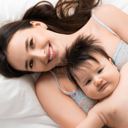 Téléchargez les photos : Belle mère heureuse en sous-vêtements bleus couchée au lit avec son petit fils plan grand angle - en image libre de droit