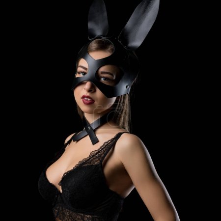 Téléchargez les photos : Femme en masque et oreilles de lapin portant un soutien-gorge en dentelle noire portrait recadré dans l'obscurité - en image libre de droit