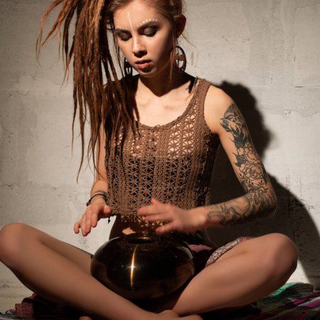 Girl with blonde dreadlocks sitting on the floor playing tapidrum view in the dark room