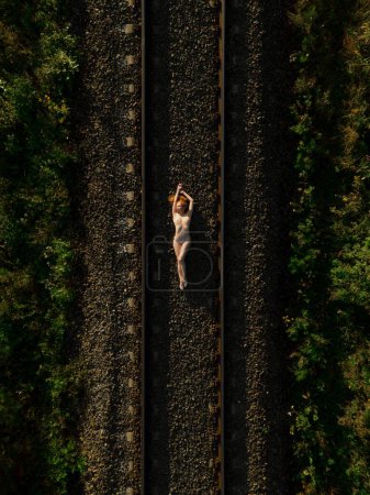 Téléchargez les photos : Vue du dessus de la femelle nue couchée sur la route ferroviaire au lever du soleil - en image libre de droit