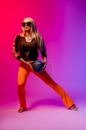 Téléchargez les photos : Corps complet de jeune femme confiante en tenue tendance et lunettes de soleil debout sur fond rose - en image libre de droit